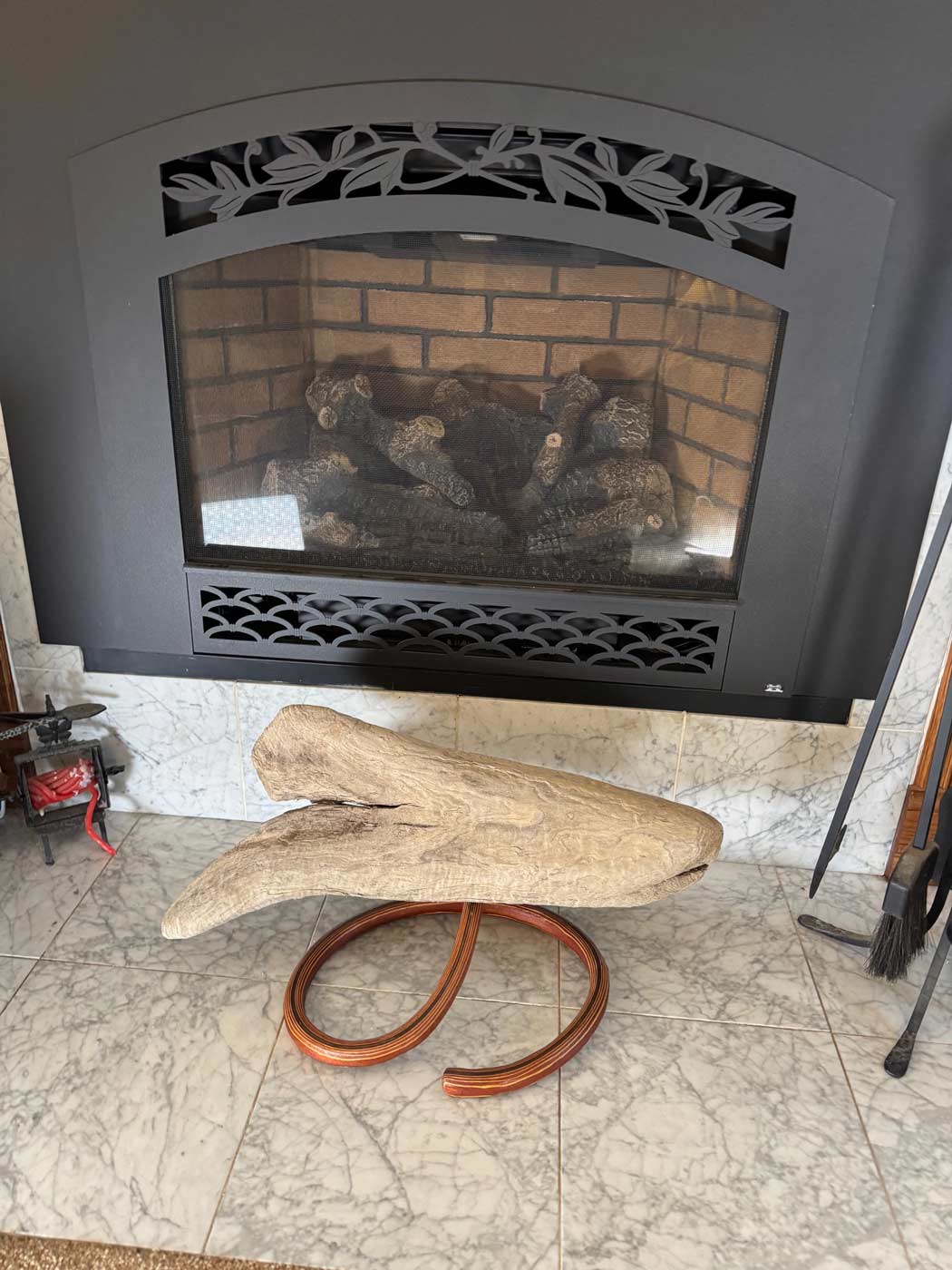 Fireplace with decorative screen and logs, featuring a mounted piece of driftwood in front.
